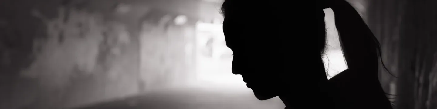 A silhouette of a woman standing against a wall in a dark alleyway.