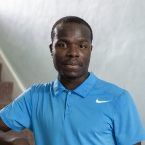 Young black man in blue polo shirt stands near stairs in homeless hostel