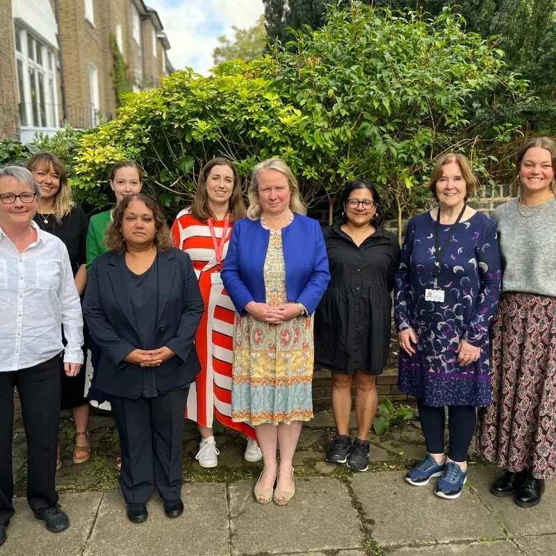 A group of people standing close together outside in a garden, smiling and looking at the camera, appearing happy and united.