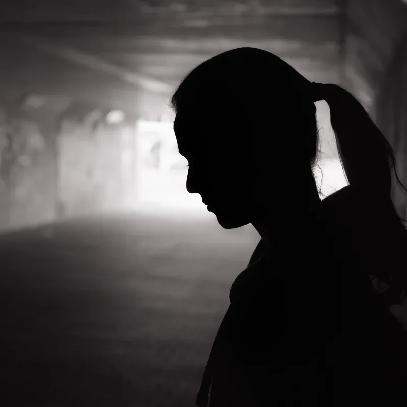 A silhouette of a woman standing against a wall in a dark alleyway.