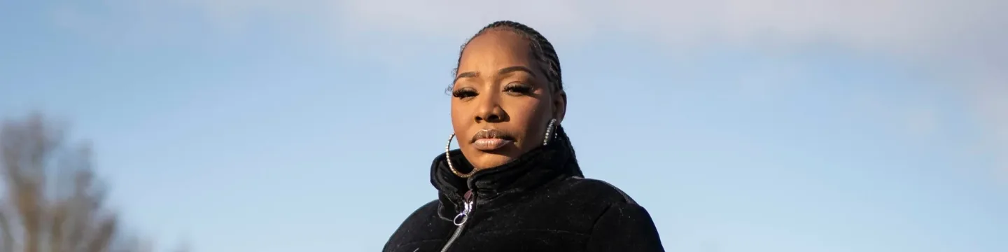 A woman stands tall in the park in a black jacket on a clear day.