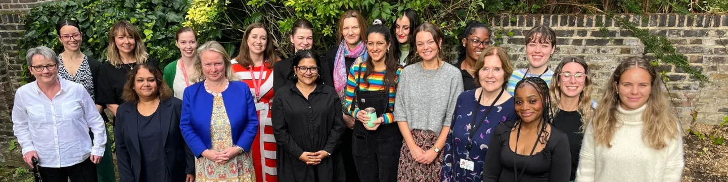 A large group of people standing close together outside in a garden, smiling and looking at the camera, appearing happy and united.