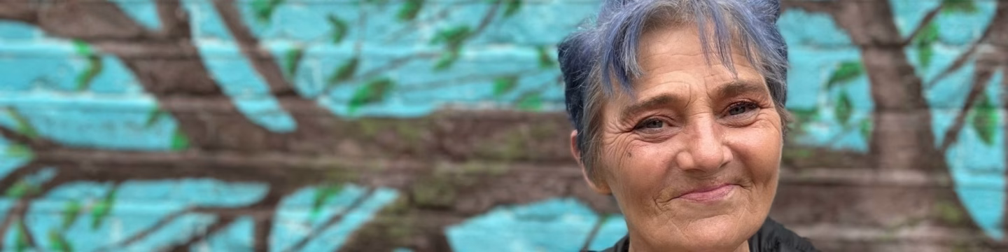 A woman is standing, smiling, with a colourful backdrop.