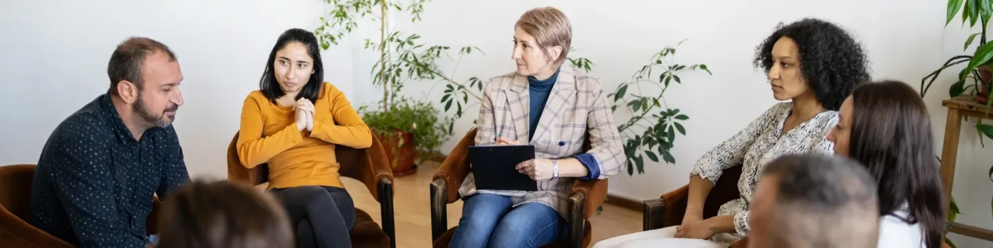 A group of people seated in a room, chatting to one another.