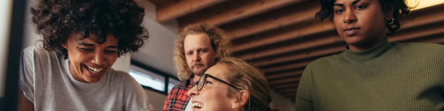 Four people chatting together at a desk in an office.