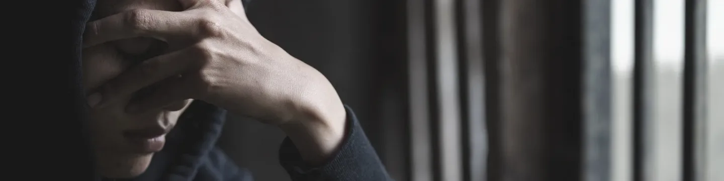 A young woman wearing a black hoodie has her head in her hands in a dark room.