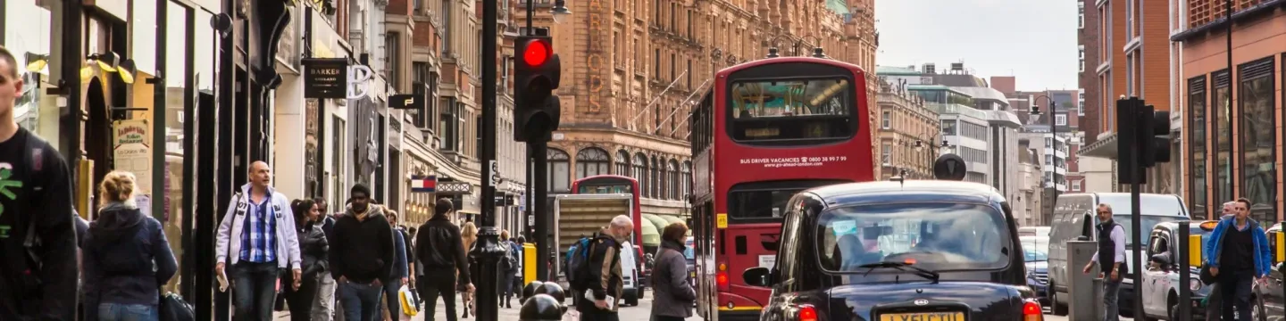 A busy street in central London filled with cars, buses, and people bustling along the sidewalks, capturing the city's vibrant atmosphere.