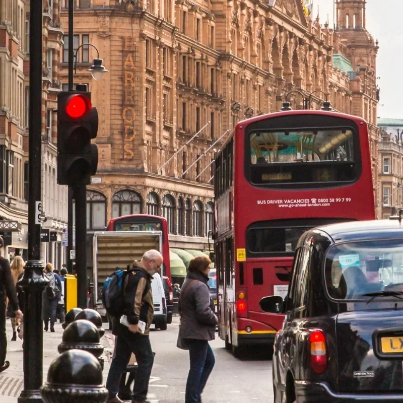 A busy street in central London filled with cars, buses, and people bustling along the sidewalks, capturing the city's vibrant atmosphere.