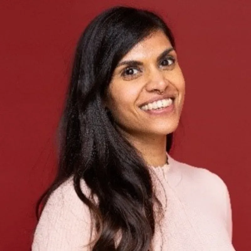 A A woman with long black hair wearing a light pink jumper smiles warmly.