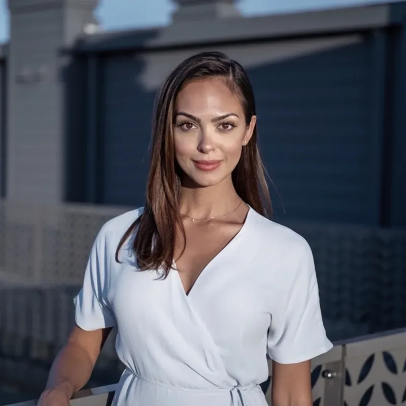 A woman wearing a white dress poses on a balcony.