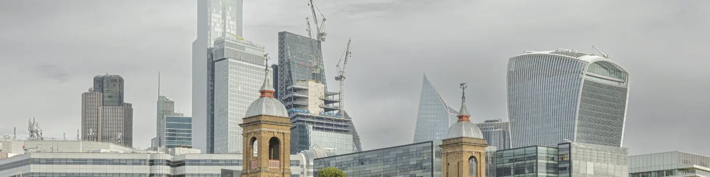 A London skyline on a cloudy day, featuring iconic landmarks like the walkie-talkie building against a backdrop of grey clouds.