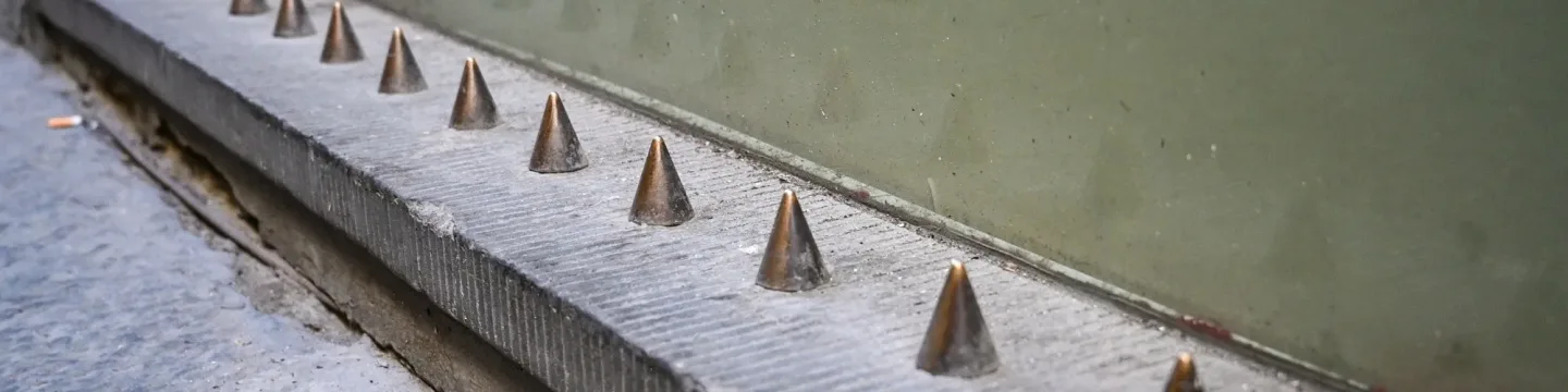 A row of sharp spikes protruding from a wall next to a building.