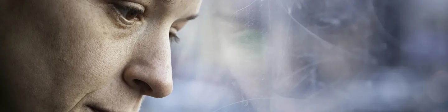 A woman sits quietly, staring at a frosted glass window, her expression thoughtful and distant.