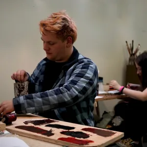 Young man with plaid shirt does printing art on a table
