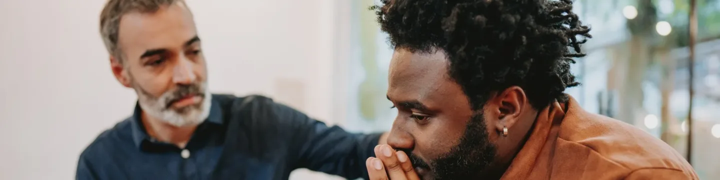 two men in a support group with an older man giving a black younger man encouragement