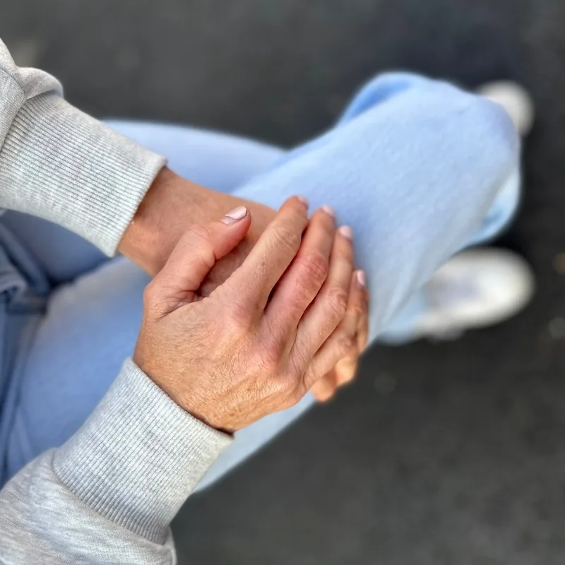 A woman sitting with her hands resting on her knees, displaying a relaxed posture.