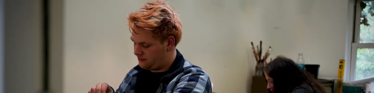 A man and woman are partaking in a screen-printing project, working together in an art studio with tools nearby.