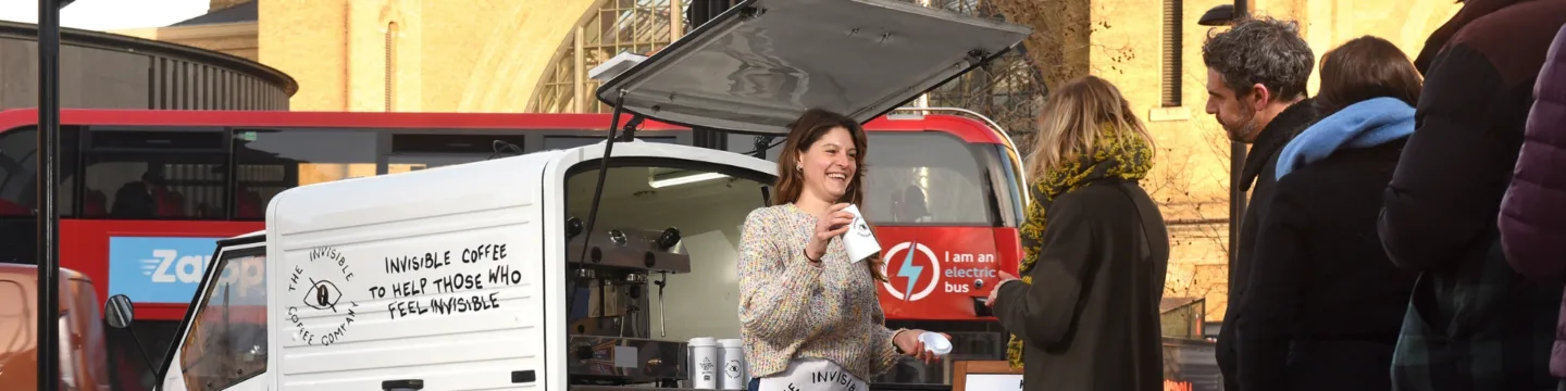 A woman smiles while standing beside a tuk-tuk, happily serving a customer.