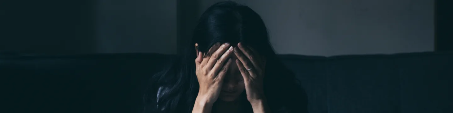 A woman sits on a sofa, covering her face with her hands, conveying deep distress and emotional turmoil.
