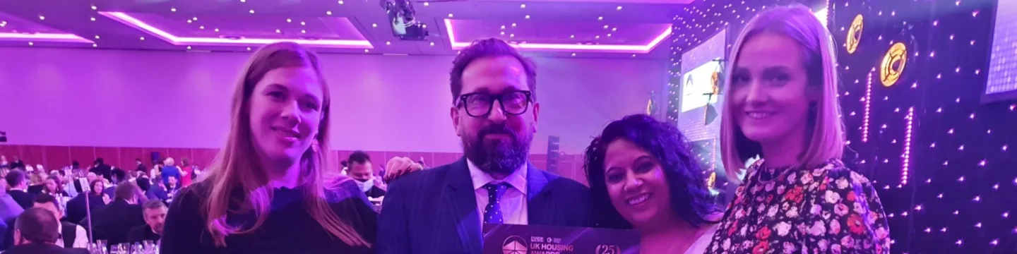 Four people in a room, with a man and woman proudly displaying a certificate together.