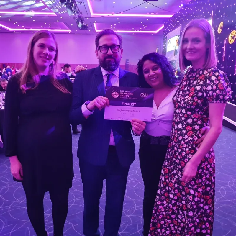 Four people in a room, with a man and woman proudly displaying a certificate together.