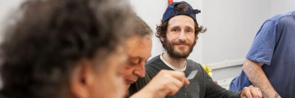 homeless man in cap eats dinner and stares at camera