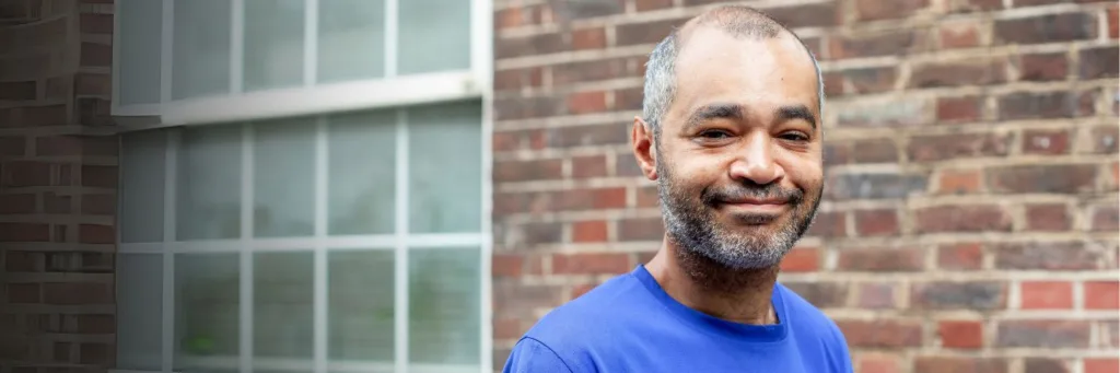 happy man smiles at camera outside brick wall