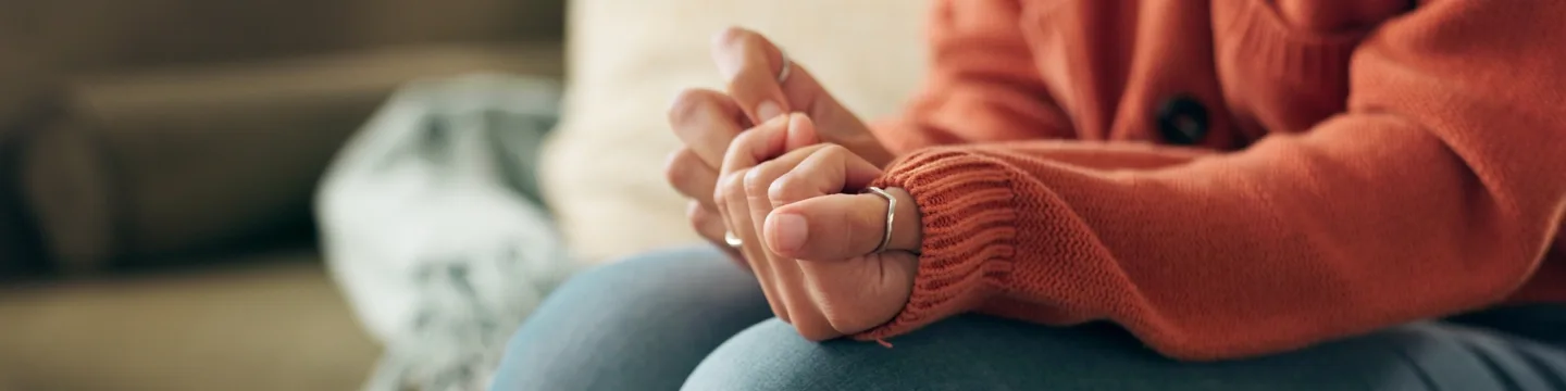 Close-up of a woman’s hands clasped tightly in her lap, showing signs of anxiety and stress during a trauma therapy or mental health counselling session.