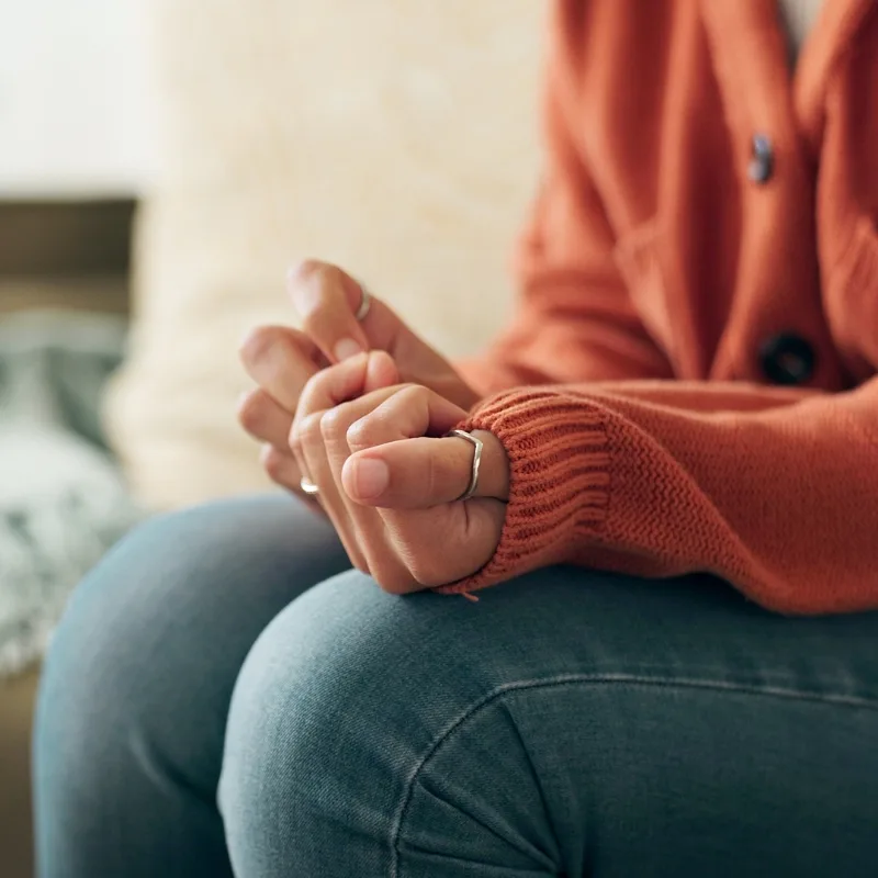 Close-up of a woman’s hands clasped tightly in her lap, showing signs of anxiety and stress during a trauma therapy or mental health counselling session.