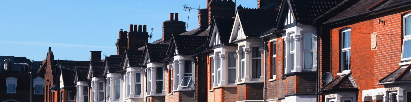 A row of red brick houses with chimneys, set against a clear blue sky.