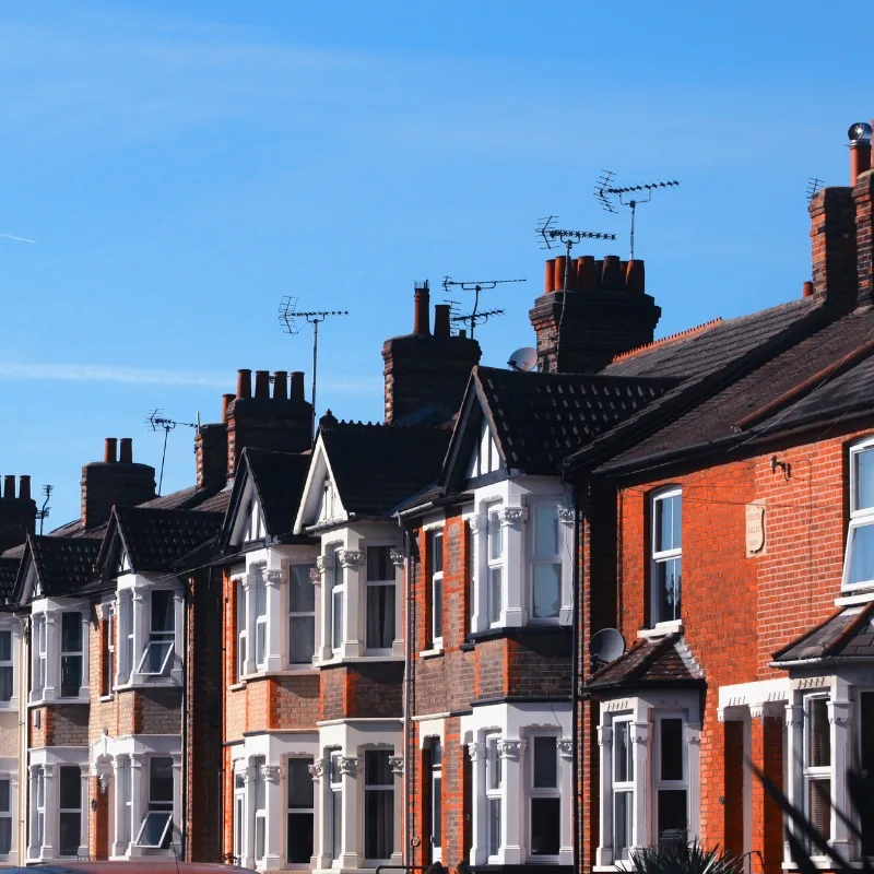 A row of red brick houses with chimneys, set against a clear blue sky.