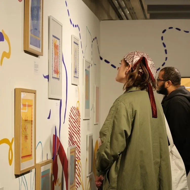 Lady in green coat and bandana looks at artwork on the gallery wall.