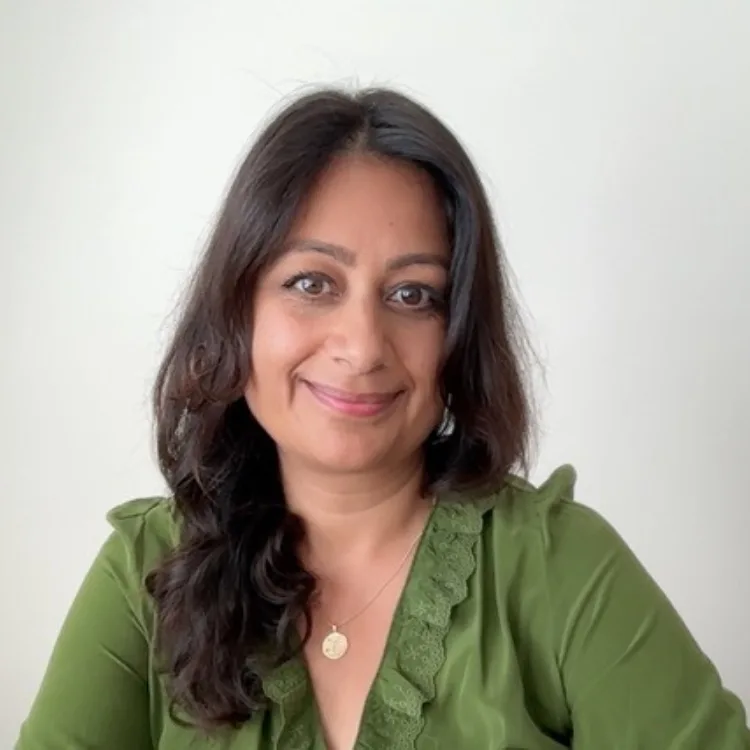 Woman with long dark hair smiles softly against a plain background. She wears a green top and a necklace.