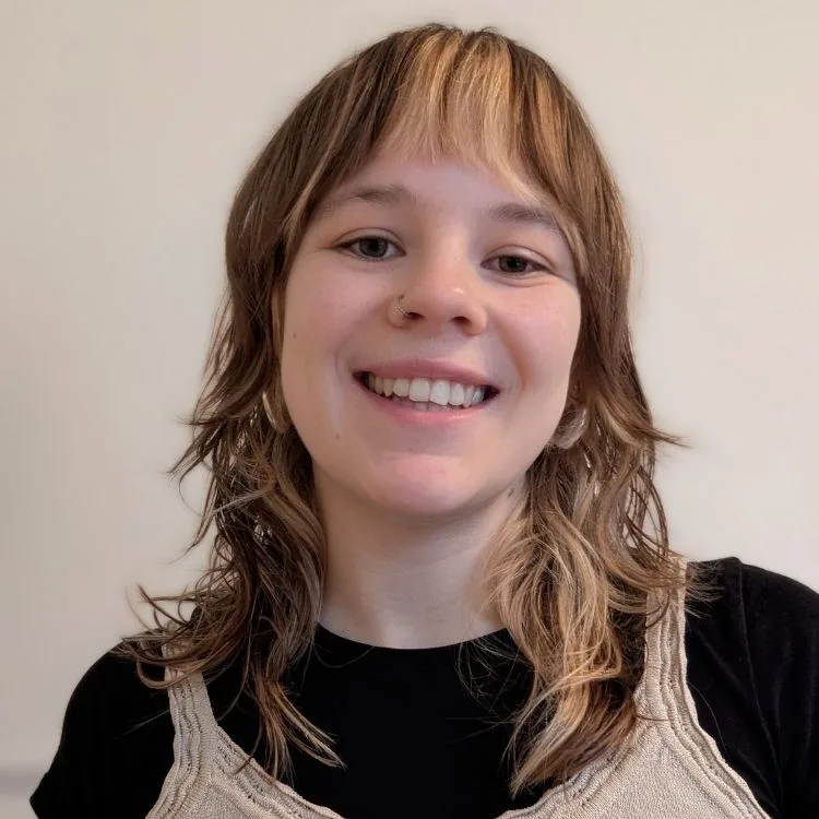 Young woman smiles with a white wall behind her.
