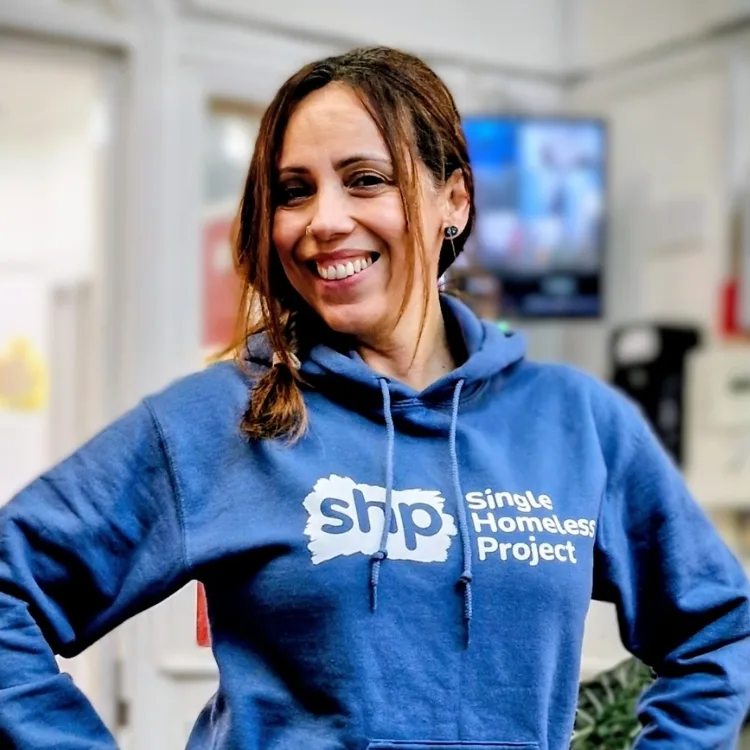 Woman smiling and wearing a blue hoodie, standing indoors with a blurred background.